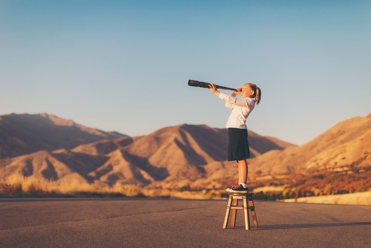 A young girl on a stool using a telescope