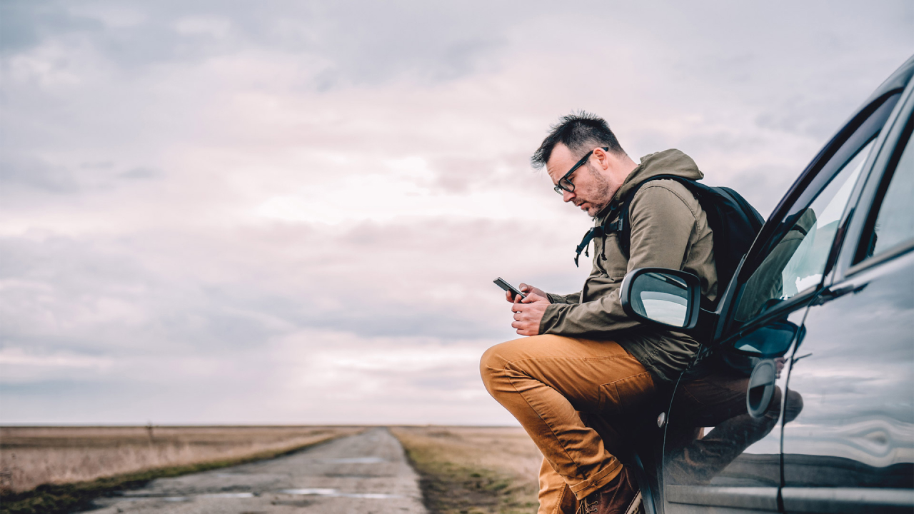 man looking at his phone sat on a car bonnet