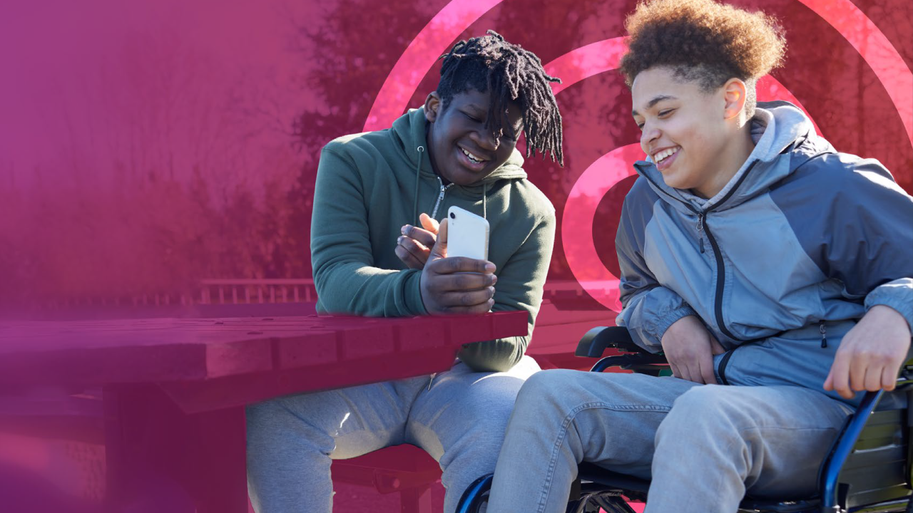 Two teenage boys smiling and looking at a phone together